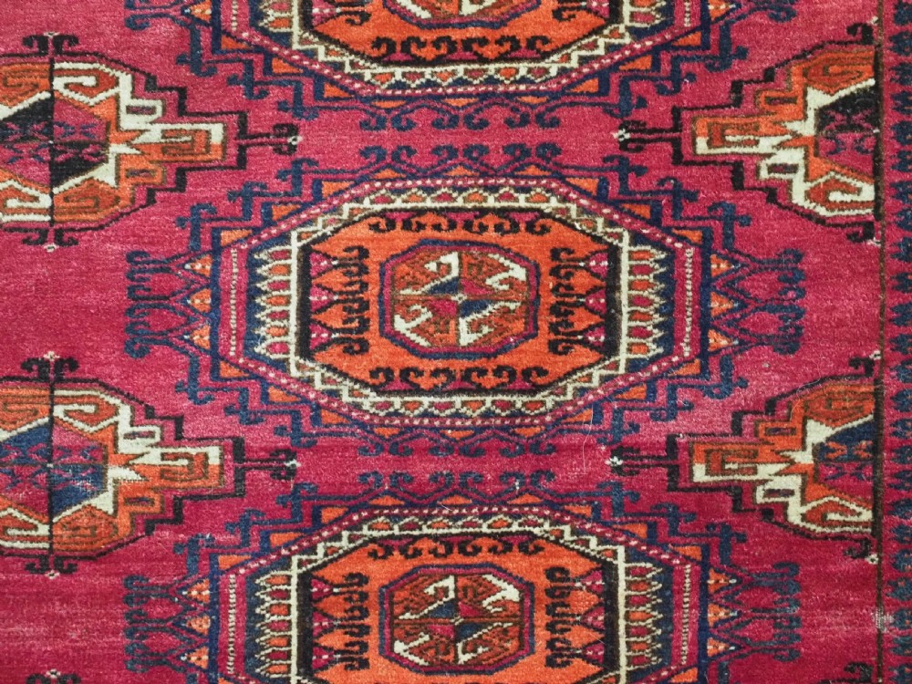 A rectangular hand-knotted crimson red Turkmen chuval featuring nine central octagonal Salor guls framed by ornate geometric borders and a decorative lower elem panel. View X