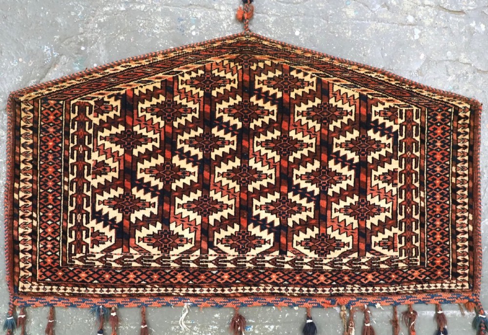 A pentagonal hand-knotted antique Yomut Turkmen Asmalyk wool textile featuring geometric lattice motifs in red, dark brown, and cream with hanging multi-coloured tassels along the lower edge. View II