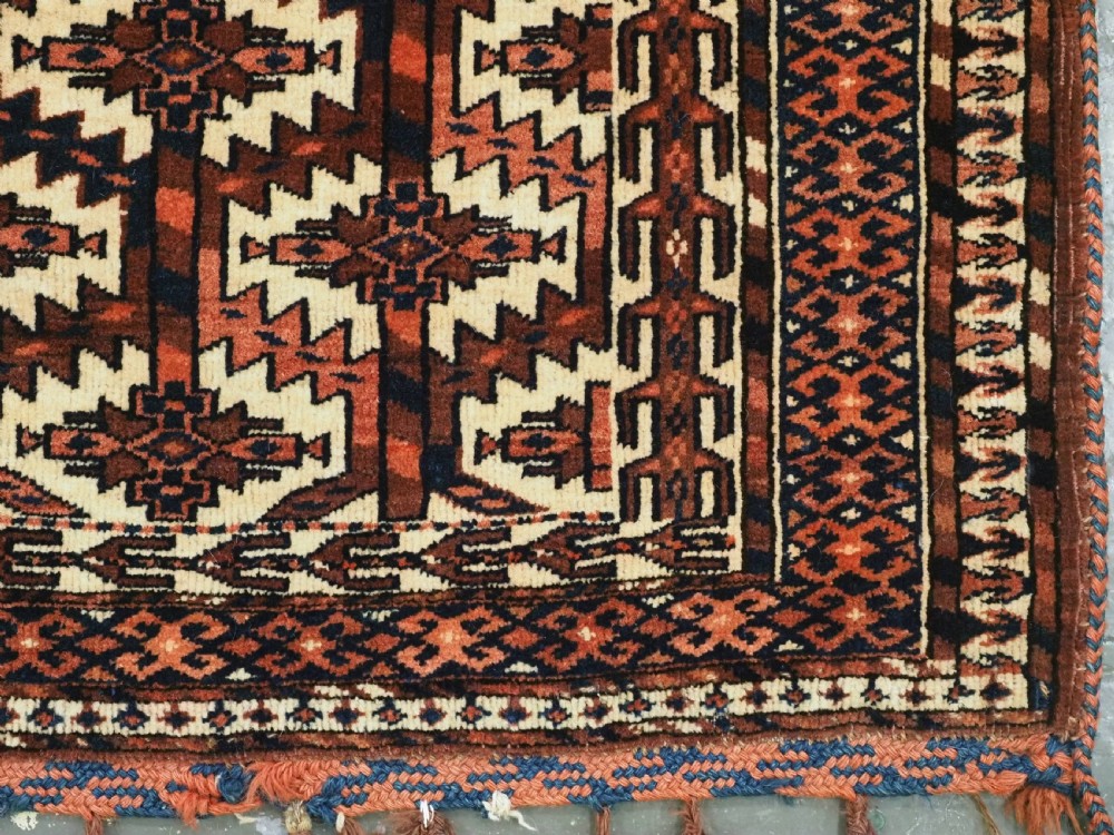 A pentagonal hand-knotted antique Yomut Turkmen Asmalyk wool textile featuring geometric lattice motifs in red, dark brown, and cream with hanging multi-coloured tassels along the lower edge. View VII