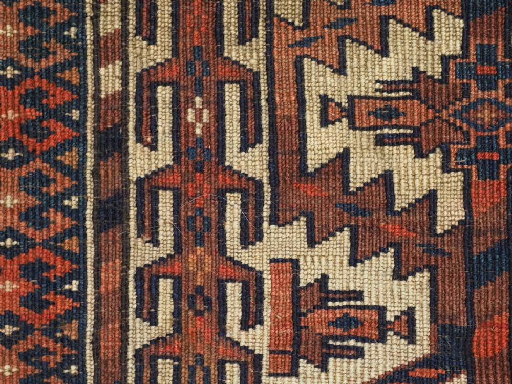 A pentagonal hand-knotted antique Yomut Turkmen Asmalyk wool textile featuring geometric lattice motifs in red, dark brown, and cream with hanging multi-coloured tassels along the lower edge. View VIII