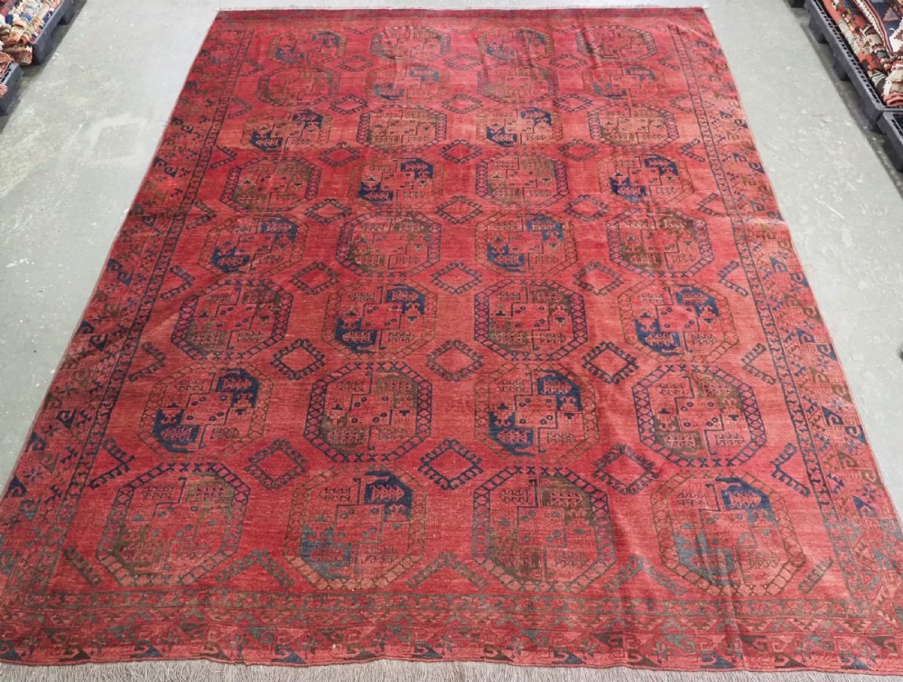 An antique hand-knotted Ersari wool carpet featuring repeating octagonal gol motifs in blue and green on a rich warm red field.