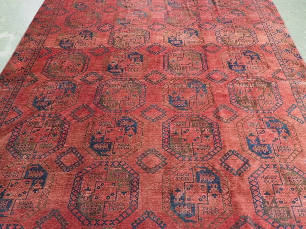 An antique hand-knotted Ersari wool carpet featuring repeating octagonal gol motifs in blue and green on a rich warm red field. View III