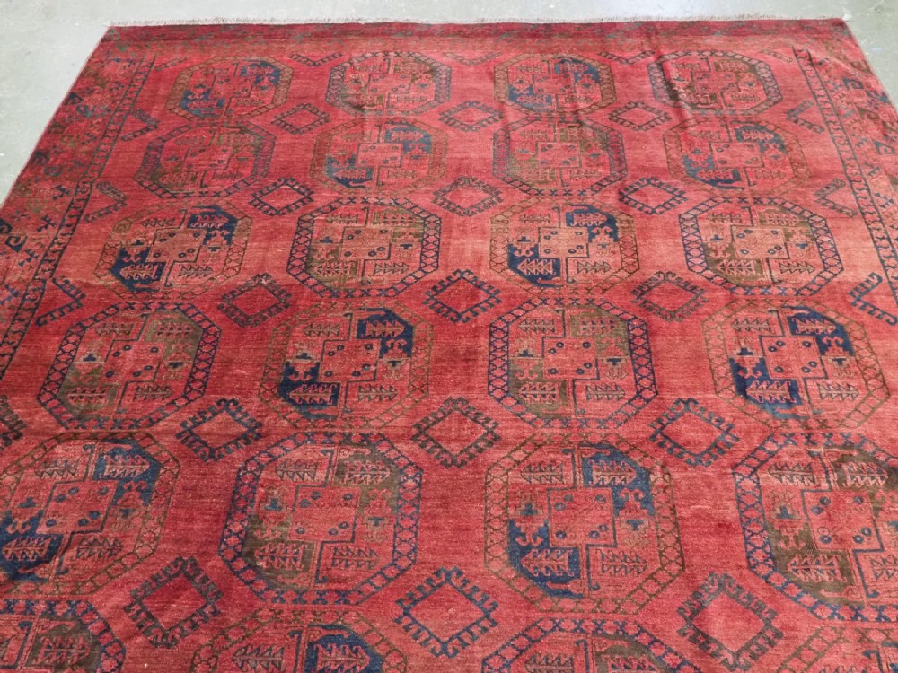 An antique hand-knotted Ersari wool carpet featuring repeating octagonal gol motifs in blue and green on a rich warm red field. View IV