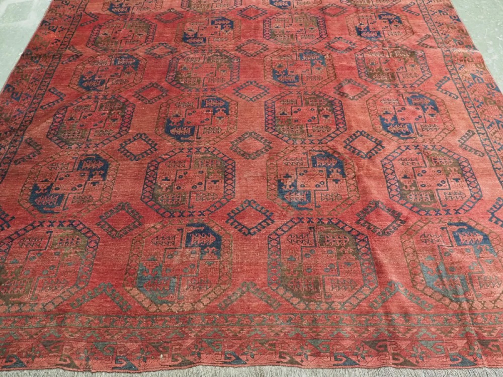 An antique hand-knotted Ersari wool carpet featuring repeating octagonal gol motifs in blue and green on a rich warm red field. View V