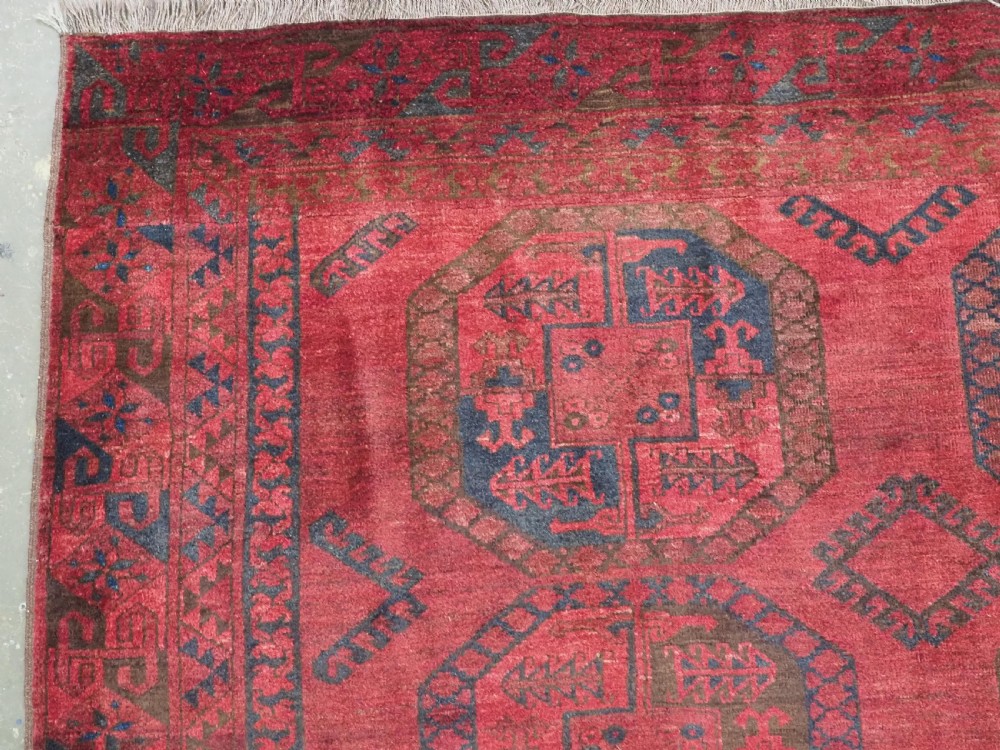 An antique hand-knotted Ersari wool carpet featuring repeating octagonal gol motifs in blue and green on a rich warm red field. View VI