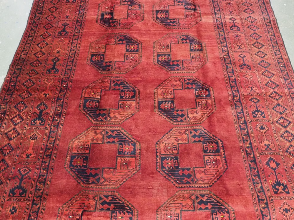 An antique hand-knotted Afghan Ersari wool carpet featuring repeating octagonal gul motifs across a deep red field framed by geometric borders. View IV