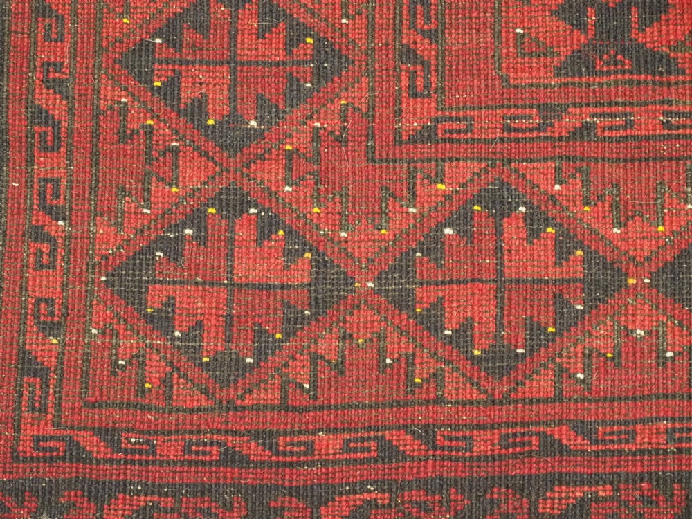 An antique hand-knotted Afghan Ersari wool carpet featuring repeating octagonal gul motifs across a deep red field framed by geometric borders. View X