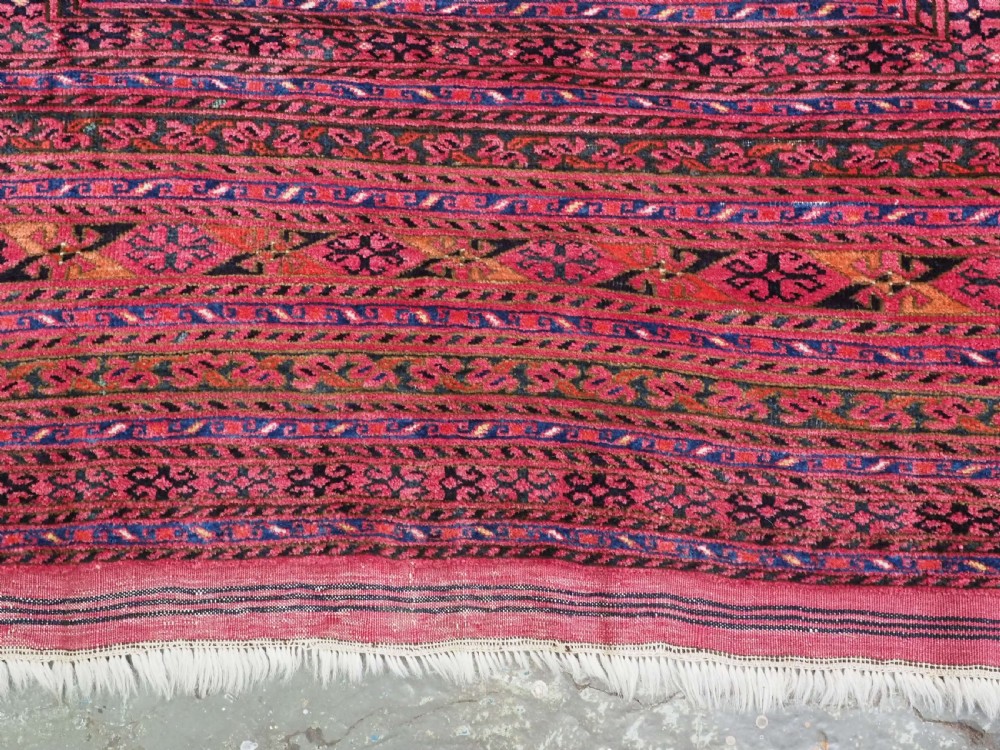 An elongated antique Afghan Ersari wool kelleh carpet featuring intricate geometric repeating motifs in shades of red, crimson, and black. View IX
