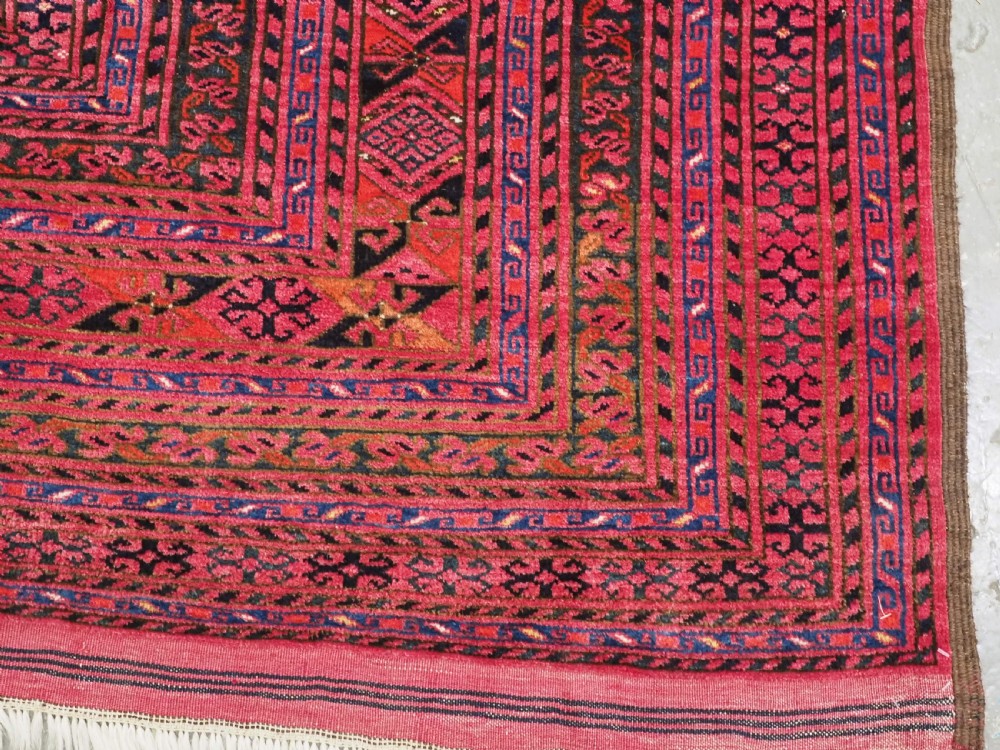 An elongated antique Afghan Ersari wool kelleh carpet featuring intricate geometric repeating motifs in shades of red, crimson, and black. View X