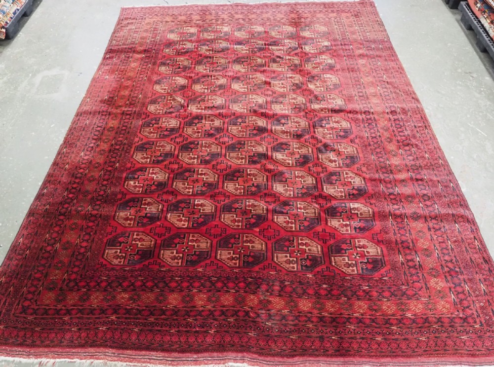 An antique Afghan Turkmen wool carpet in deep red tones featuring a repeating grid pattern of octagonal gul motifs framed by geometric borders.