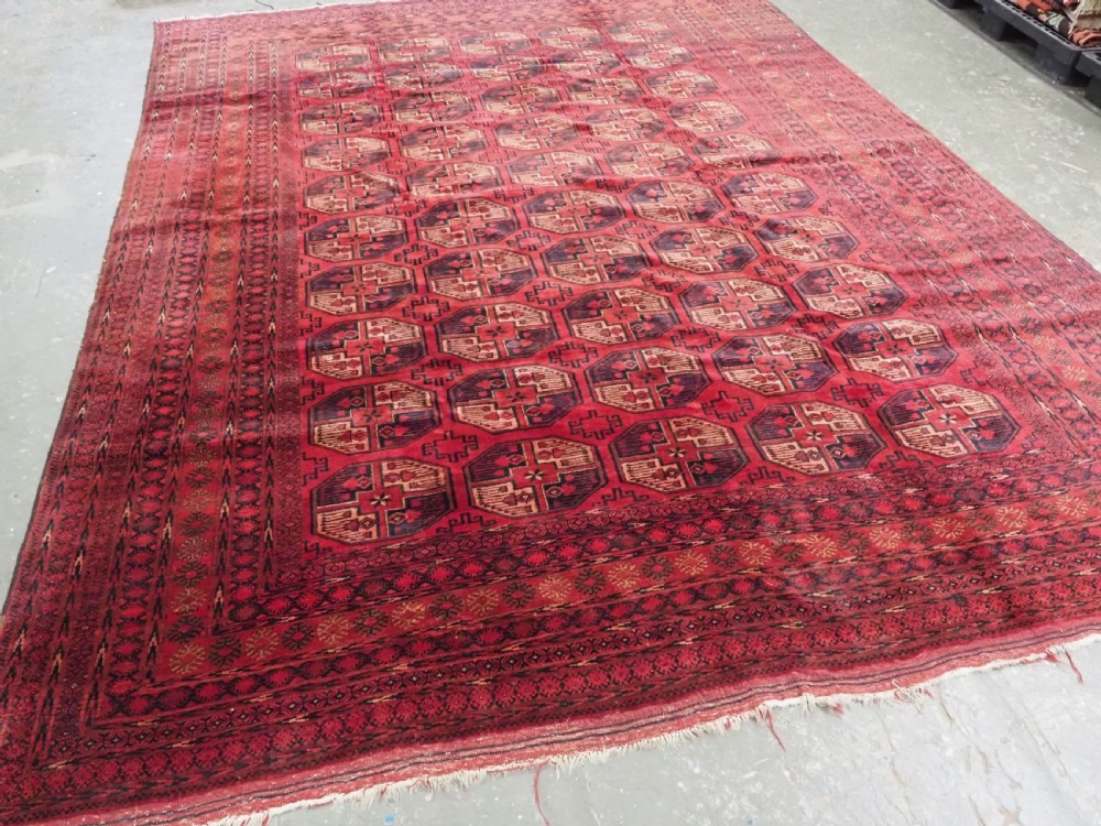 An antique Afghan Turkmen wool carpet in deep red tones featuring a repeating grid pattern of octagonal gul motifs framed by geometric borders. View II