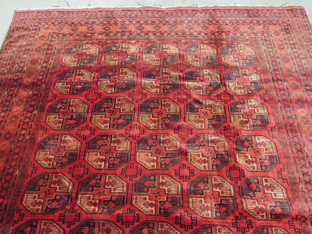 An antique Afghan Turkmen wool carpet in deep red tones featuring a repeating grid pattern of octagonal gul motifs framed by geometric borders. View III