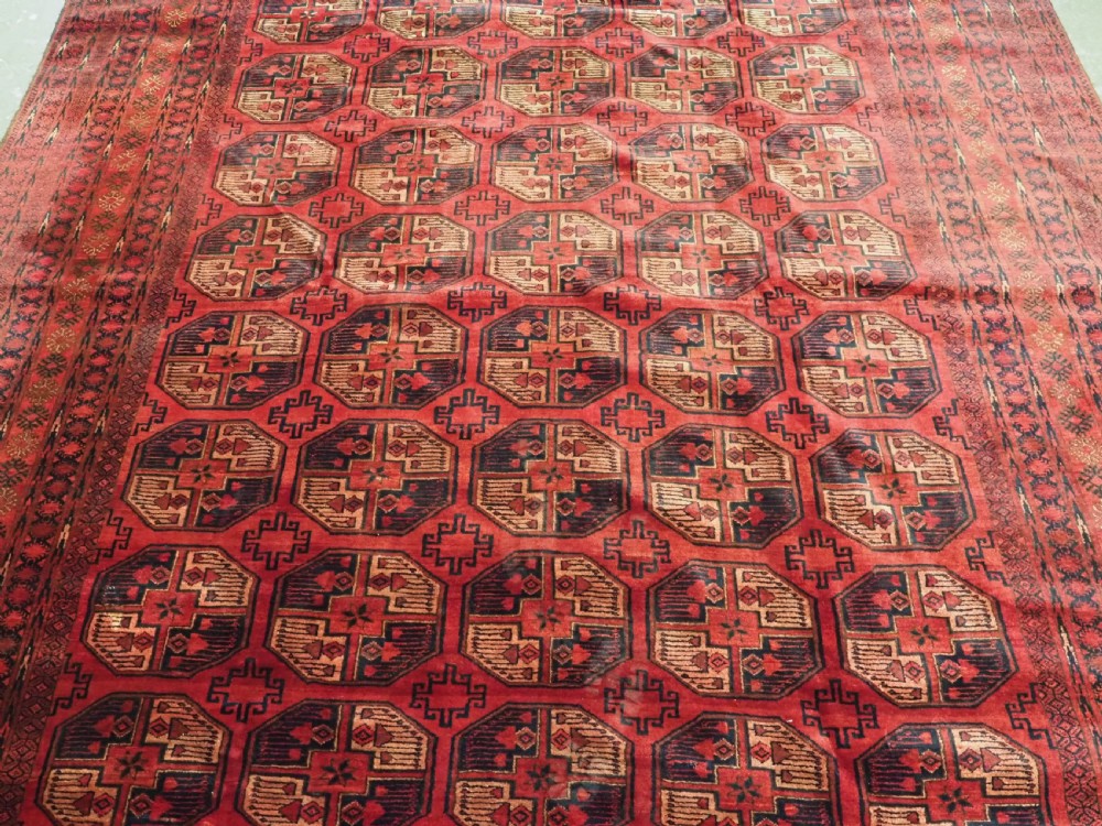 An antique Afghan Turkmen wool carpet in deep red tones featuring a repeating grid pattern of octagonal gul motifs framed by geometric borders. View IV