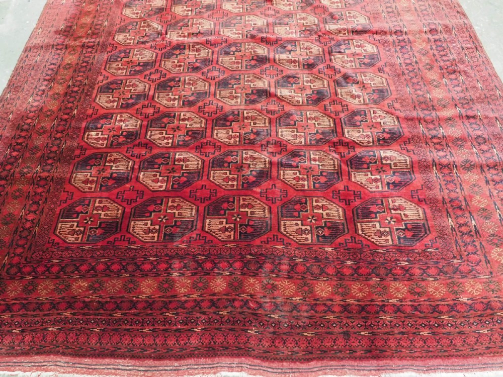 An antique Afghan Turkmen wool carpet in deep red tones featuring a repeating grid pattern of octagonal gul motifs framed by geometric borders. View V