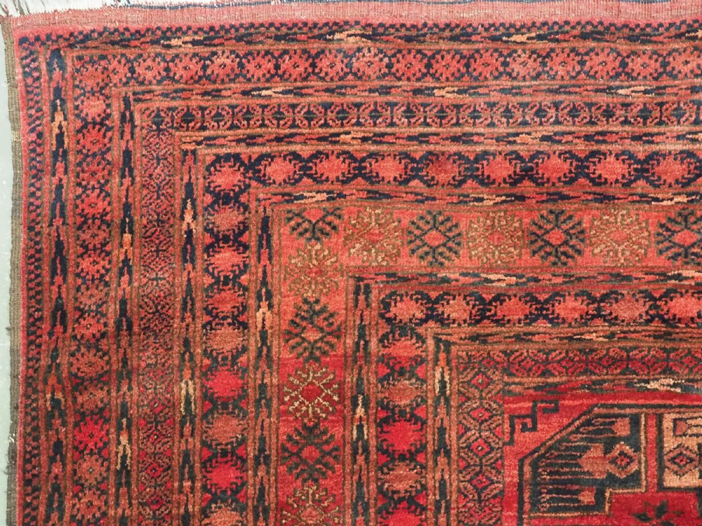 An antique Afghan Turkmen wool carpet in deep red tones featuring a repeating grid pattern of octagonal gul motifs framed by geometric borders. View VI
