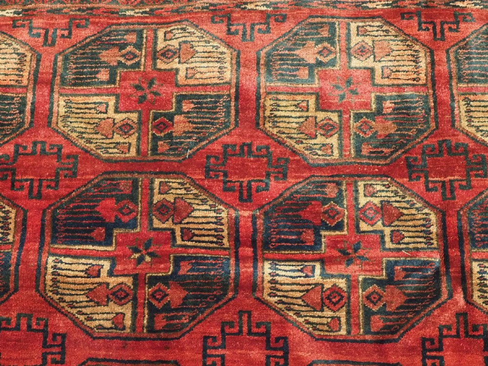 An antique Afghan Turkmen wool carpet in deep red tones featuring a repeating grid pattern of octagonal gul motifs framed by geometric borders. View VIII