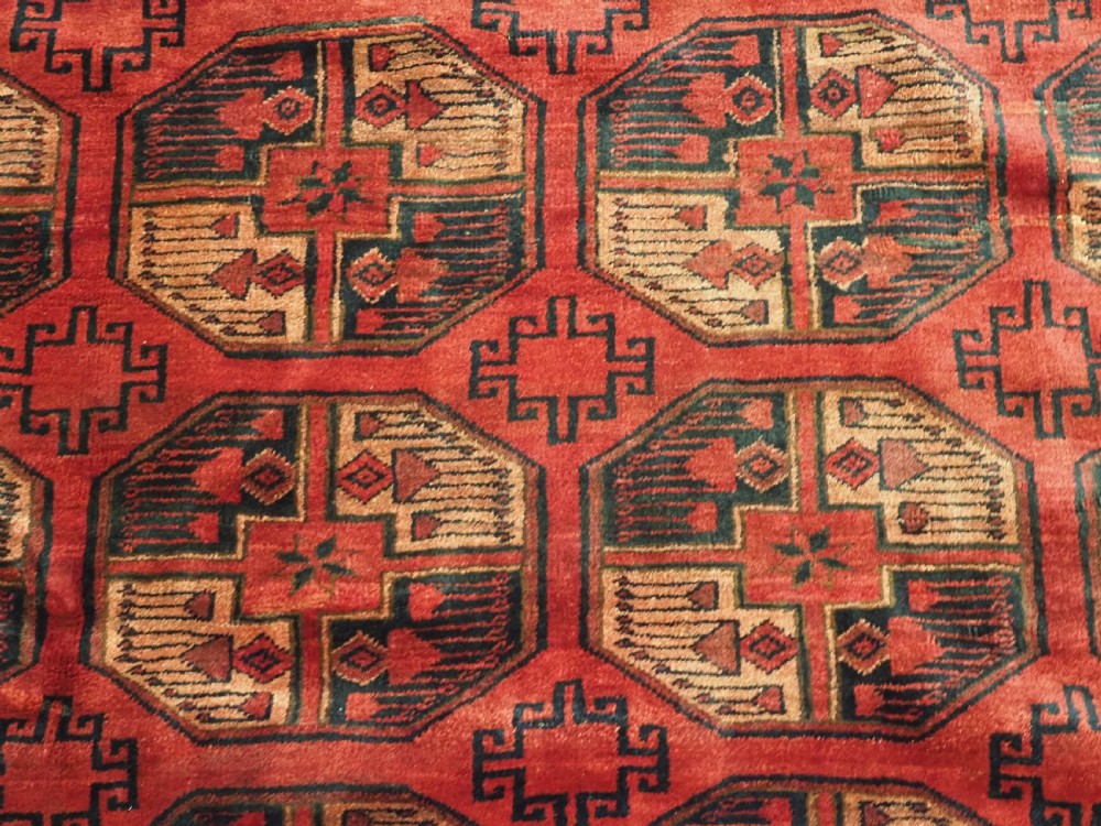 An antique Afghan Turkmen wool carpet in deep red tones featuring a repeating grid pattern of octagonal gul motifs framed by geometric borders. View IX