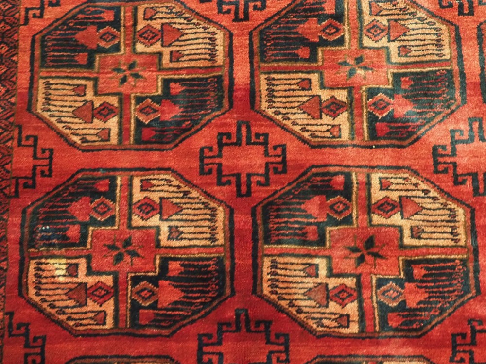An antique Afghan Turkmen wool carpet in deep red tones featuring a repeating grid pattern of octagonal gul motifs framed by geometric borders. View X