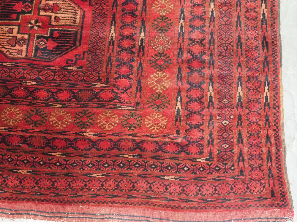 An antique Afghan Turkmen wool carpet in deep red tones featuring a repeating grid pattern of octagonal gul motifs framed by geometric borders. View XI