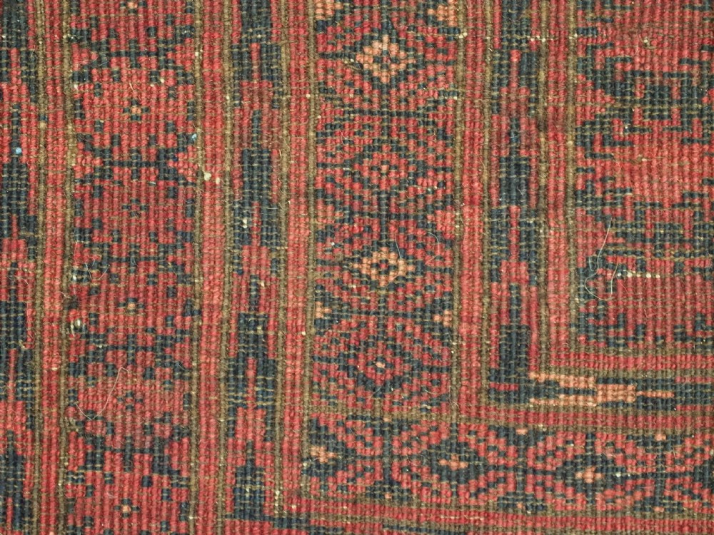 An antique Afghan Turkmen wool carpet in deep red tones featuring a repeating grid pattern of octagonal gul motifs framed by geometric borders. View XII