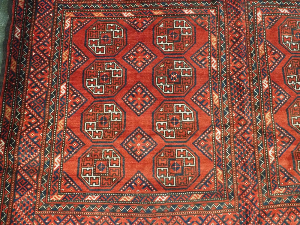 An elongated antique Turkmen Kizil Ayak wool carpet featuring multiple rectangular compartments filled with octagonal geometric guls in deep red, navy blue, and ivory tones. View X