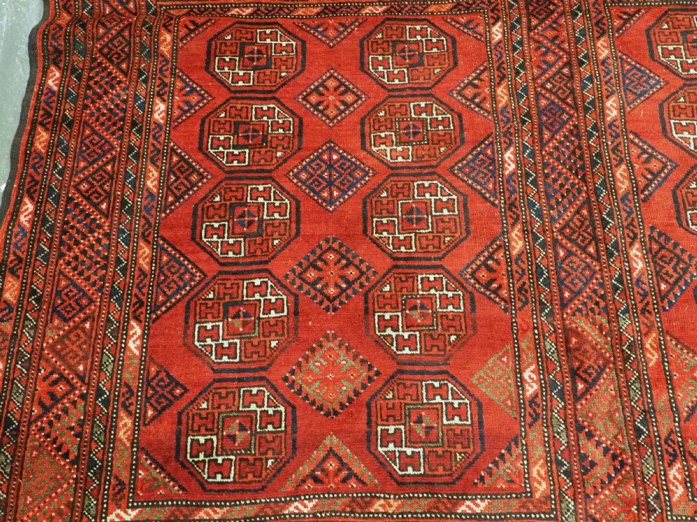 An elongated antique Turkmen Kizil Ayak wool carpet featuring multiple rectangular compartments filled with octagonal geometric guls in deep red, navy blue, and ivory tones. View XII