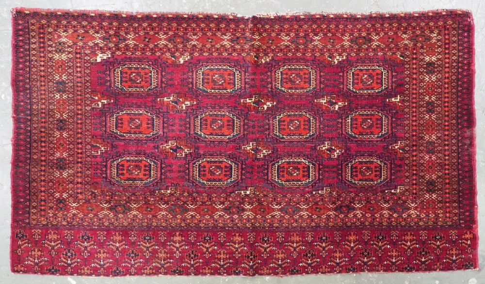 An antique woven crimson wool Tekke Turkmen chuval face featuring twelve octagonal turreted guls arranged in a rectangular grid.