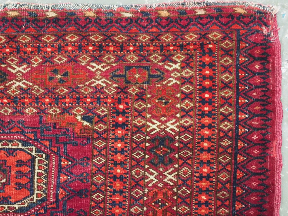 An antique woven crimson wool Tekke Turkmen chuval face featuring twelve octagonal turreted guls arranged in a rectangular grid. View X