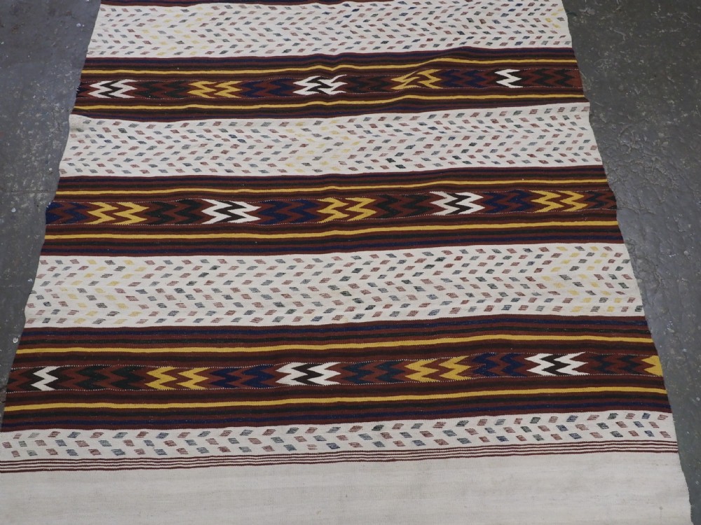 A long handwoven flatweave Central Asian kilim runner displaying cream sections alternating with dark brown, yellow, and red geometric bands with fringe at both ends. View IV