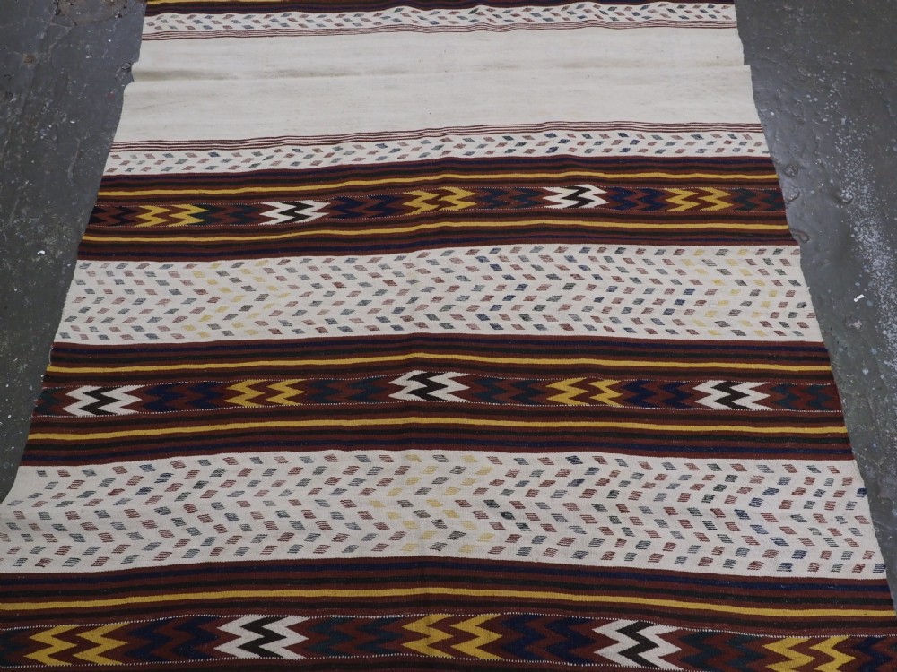 A long handwoven flatweave Central Asian kilim runner displaying cream sections alternating with dark brown, yellow, and red geometric bands with fringe at both ends. View VI