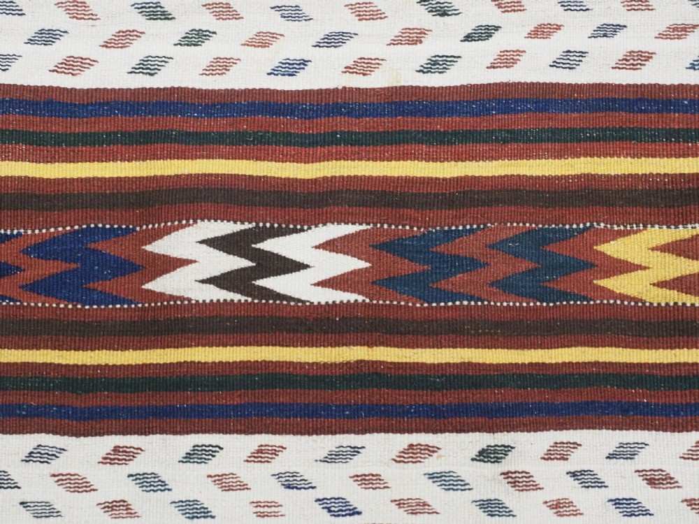 A long handwoven flatweave Central Asian kilim runner displaying cream sections alternating with dark brown, yellow, and red geometric bands with fringe at both ends. View X