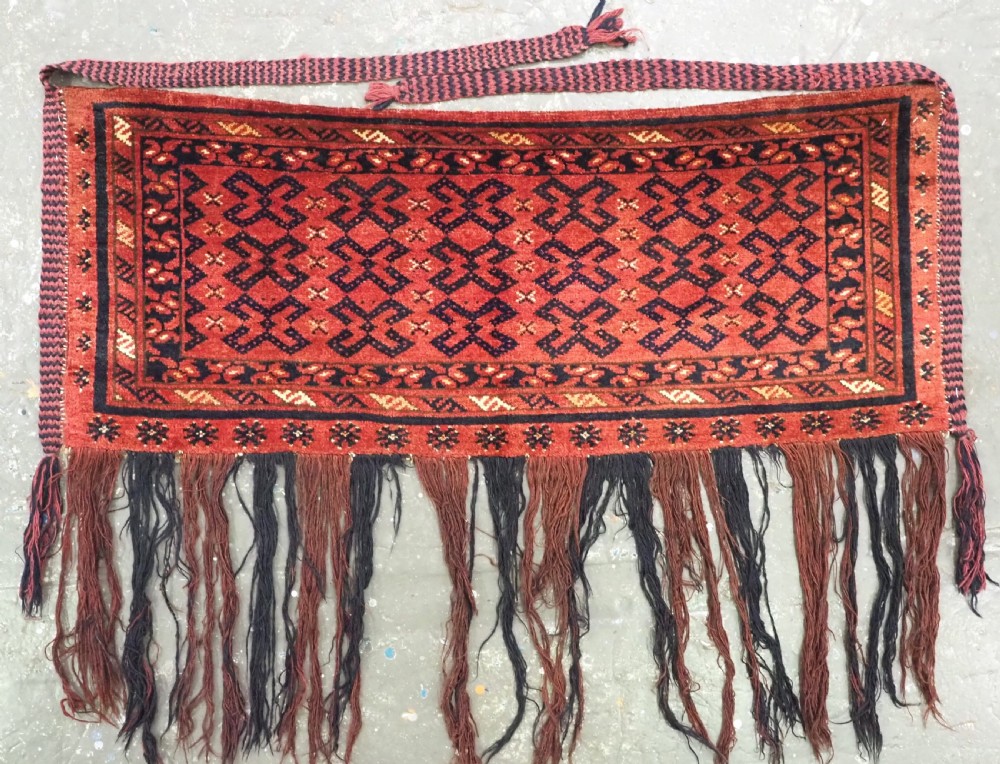 A hand-woven antique red wool Ersari Turkmen torba featuring geometric rams horn motifs, a long fringed lower edge, and braided side straps.