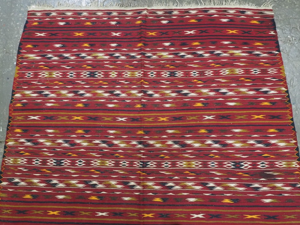 An antique flatweave Turkmen Dali kilim rug featuring horizontal bands of geometric motifs in red, cream, yellow, and dark green shades with fringed ends. View III