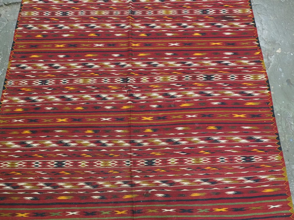 An antique flatweave Turkmen Dali kilim rug featuring horizontal bands of geometric motifs in red, cream, yellow, and dark green shades with fringed ends. View IV