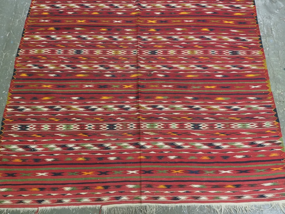 An antique flatweave Turkmen Dali kilim rug featuring horizontal bands of geometric motifs in red, cream, yellow, and dark green shades with fringed ends. View V