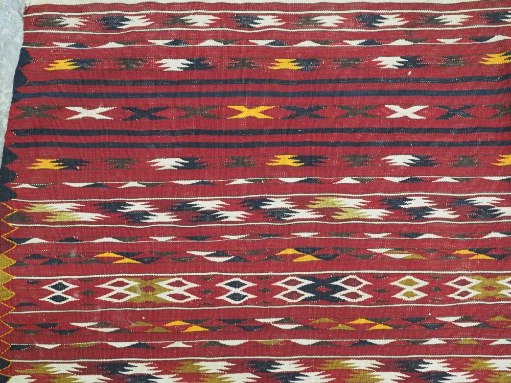 An antique flatweave Turkmen Dali kilim rug featuring horizontal bands of geometric motifs in red, cream, yellow, and dark green shades with fringed ends. View VI