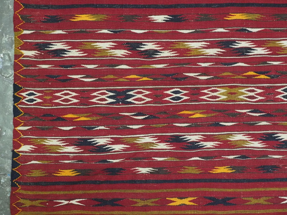 An antique flatweave Turkmen Dali kilim rug featuring horizontal bands of geometric motifs in red, cream, yellow, and dark green shades with fringed ends. View VII