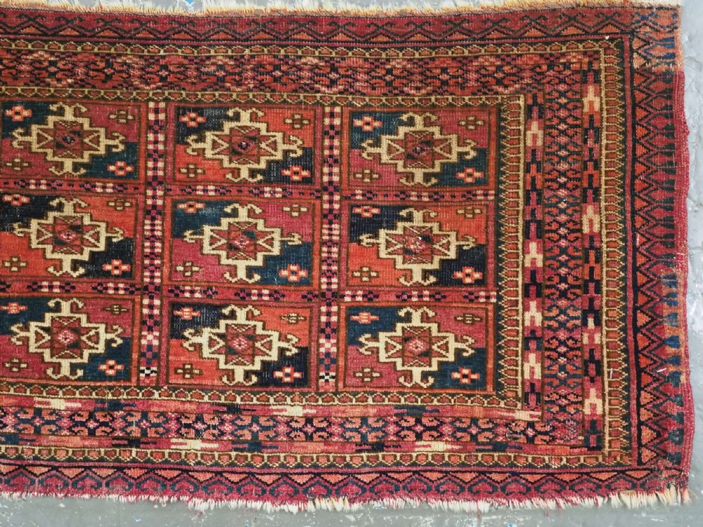 A small rectangular antique Tekke Turkmen mafrash wool panel featuring a repeating grid of geometric aina gul motifs in deep red, dark blue, and cream. View III