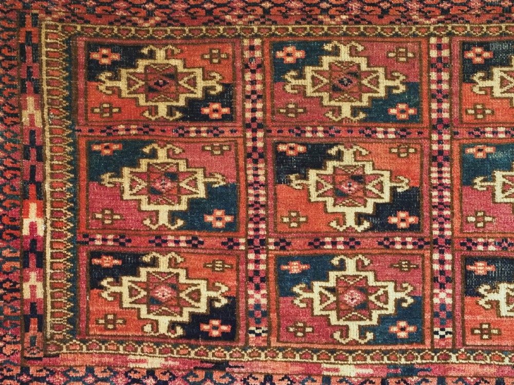 A small rectangular antique Tekke Turkmen mafrash wool panel featuring a repeating grid of geometric aina gul motifs in deep red, dark blue, and cream. View IV