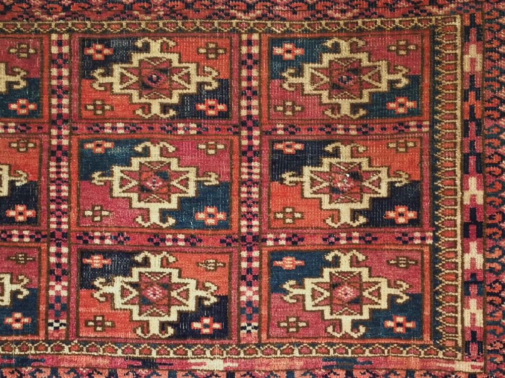 A small rectangular antique Tekke Turkmen mafrash wool panel featuring a repeating grid of geometric aina gul motifs in deep red, dark blue, and cream. View V