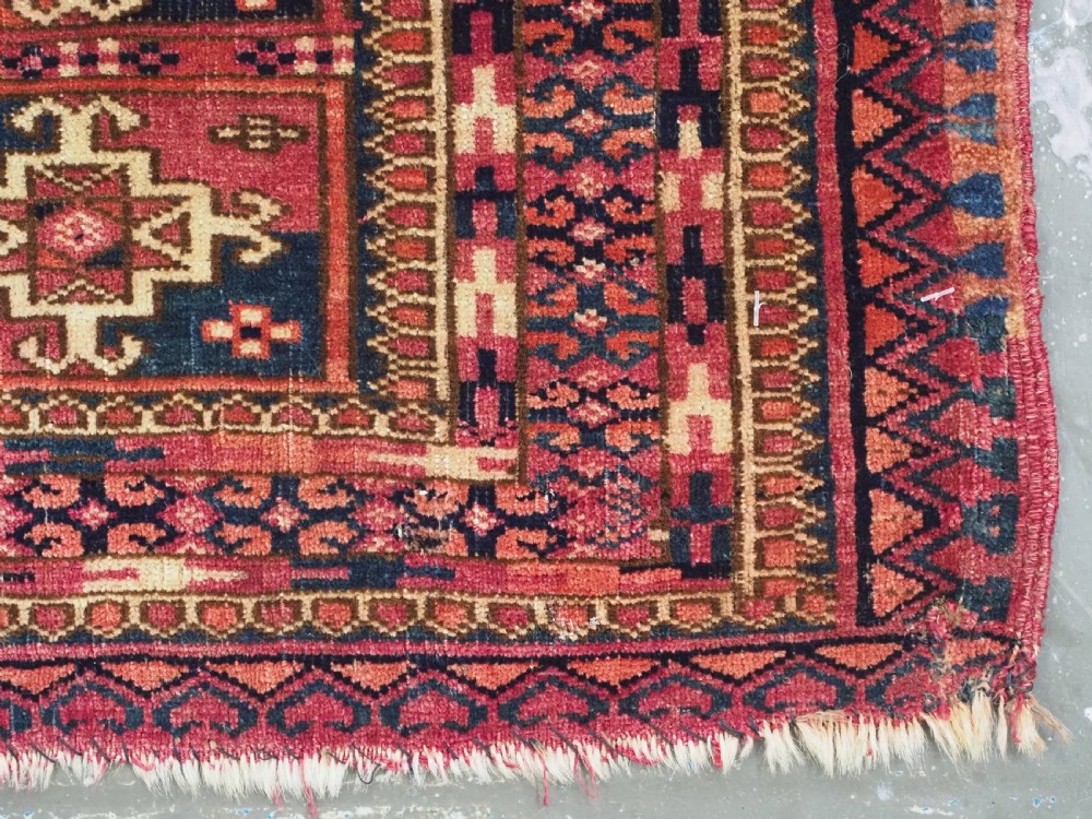 A small rectangular antique Tekke Turkmen mafrash wool panel featuring a repeating grid of geometric aina gul motifs in deep red, dark blue, and cream. View X
