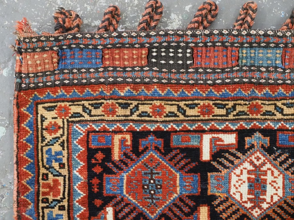 A square handwoven wool Khamseh saddlebag face featuring geometric diamond medallions in terracotta red, cream, and blue set against a dark navy ground with a multi-bordered frame. View II