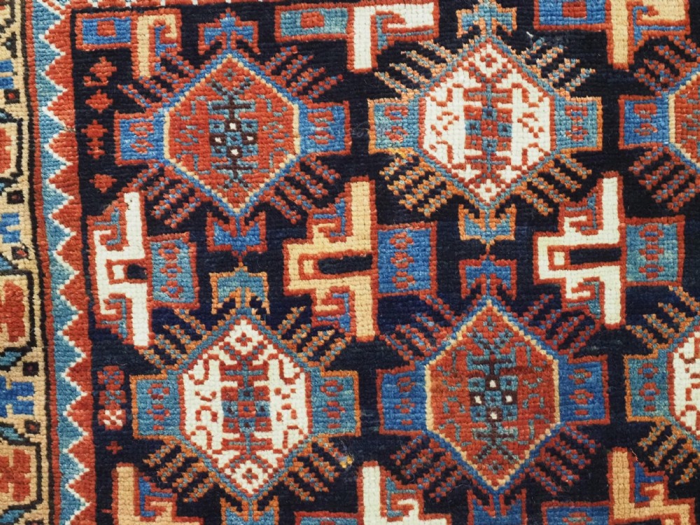 A square handwoven wool Khamseh saddlebag face featuring geometric diamond medallions in terracotta red, cream, and blue set against a dark navy ground with a multi-bordered frame. View III