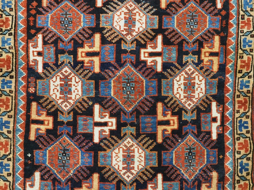 A square handwoven wool Khamseh saddlebag face featuring geometric diamond medallions in terracotta red, cream, and blue set against a dark navy ground with a multi-bordered frame. View V