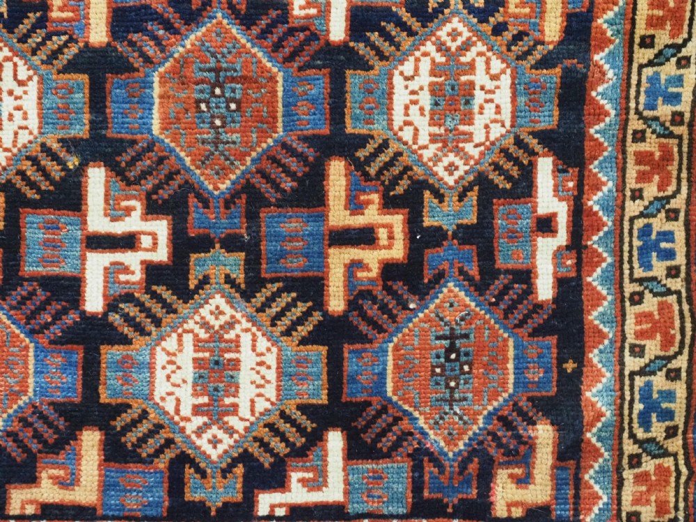 A square handwoven wool Khamseh saddlebag face featuring geometric diamond medallions in terracotta red, cream, and blue set against a dark navy ground with a multi-bordered frame. View IX