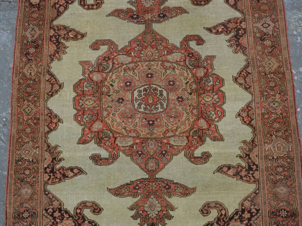 An antique hand-knotted Persian Malayer rug featuring a central terracotta medallion on a cream field with geometric patterned borders. View IV
