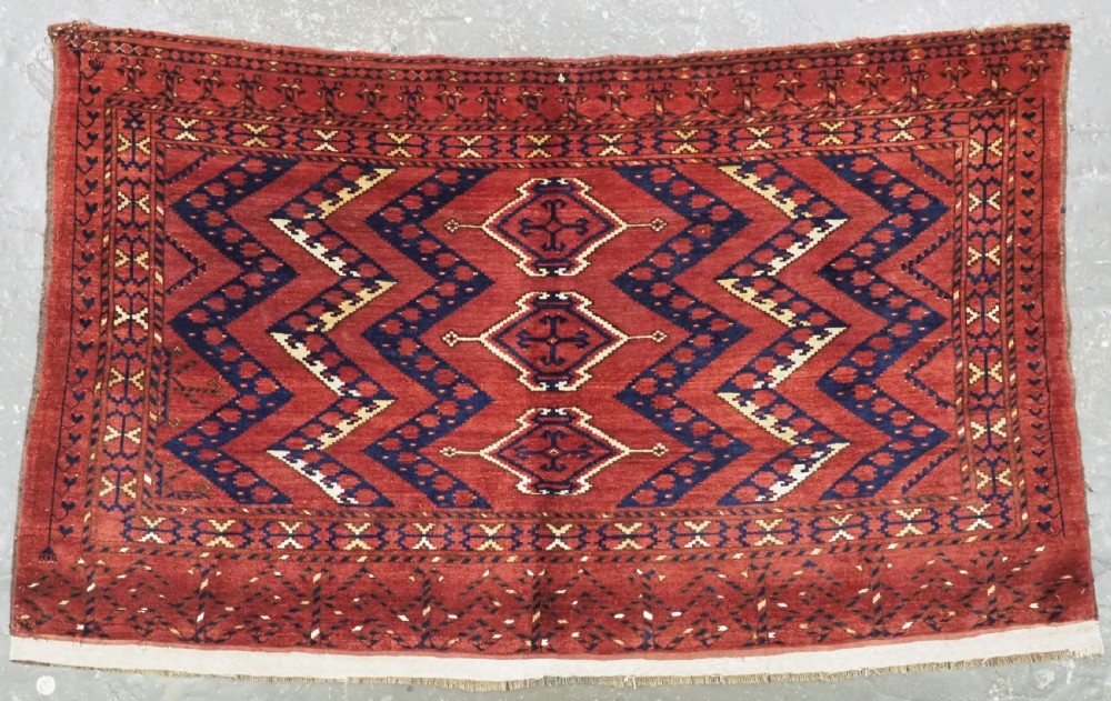 A rectangular hand-knotted wool chuval face featuring red and navy blue geometric chevron ikat patterns within decorative borders.