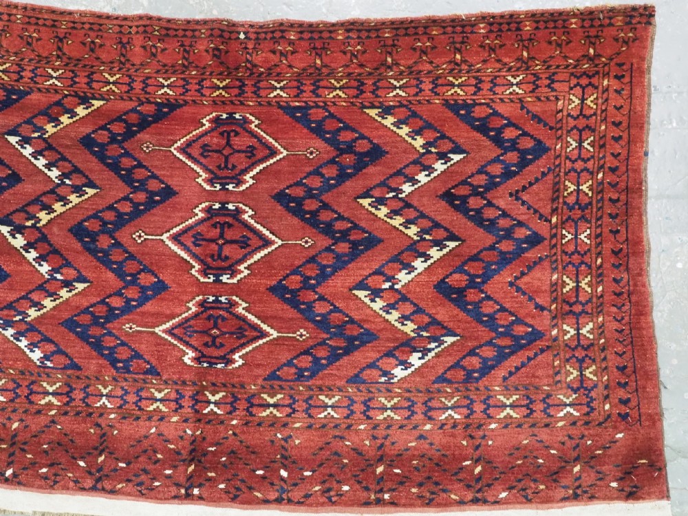 A rectangular hand-knotted wool chuval face featuring red and navy blue geometric chevron ikat patterns within decorative borders. View III