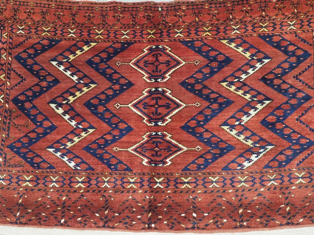 A rectangular hand-knotted wool chuval face featuring red and navy blue geometric chevron ikat patterns within decorative borders. View IV