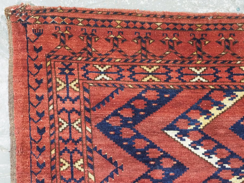 A rectangular hand-knotted wool chuval face featuring red and navy blue geometric chevron ikat patterns within decorative borders. View V